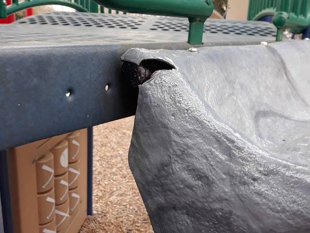 A cracked playground deck panel with an exposed pipe end